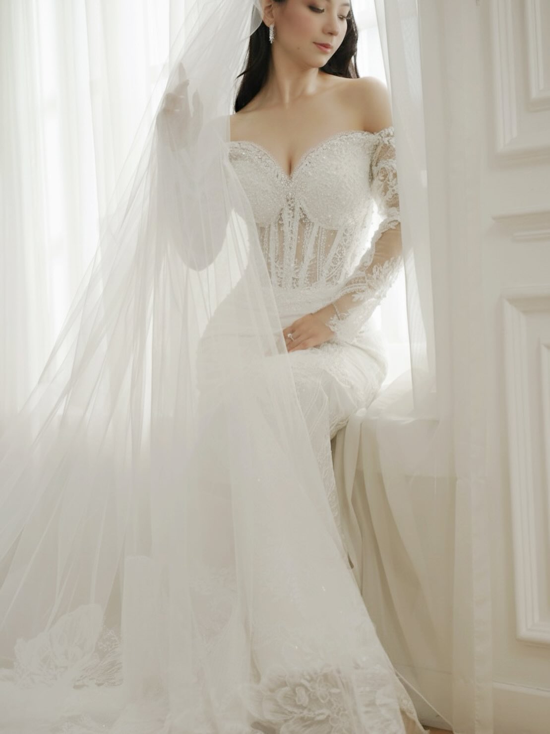 Bride in an off-shoulder lace gown holding a sheer veil by CELRA