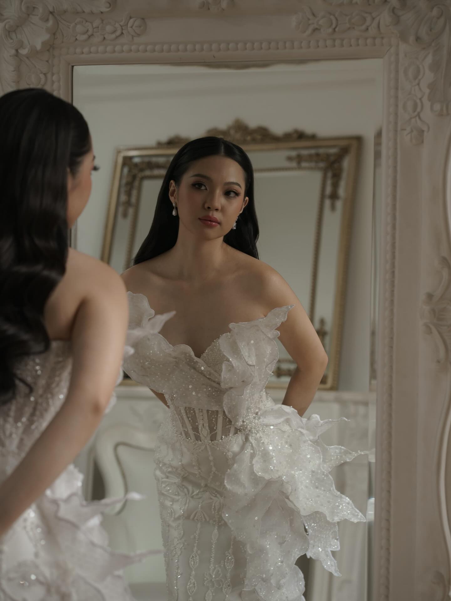Bride in a ruffled lace gown looking into a mirror by CELRA