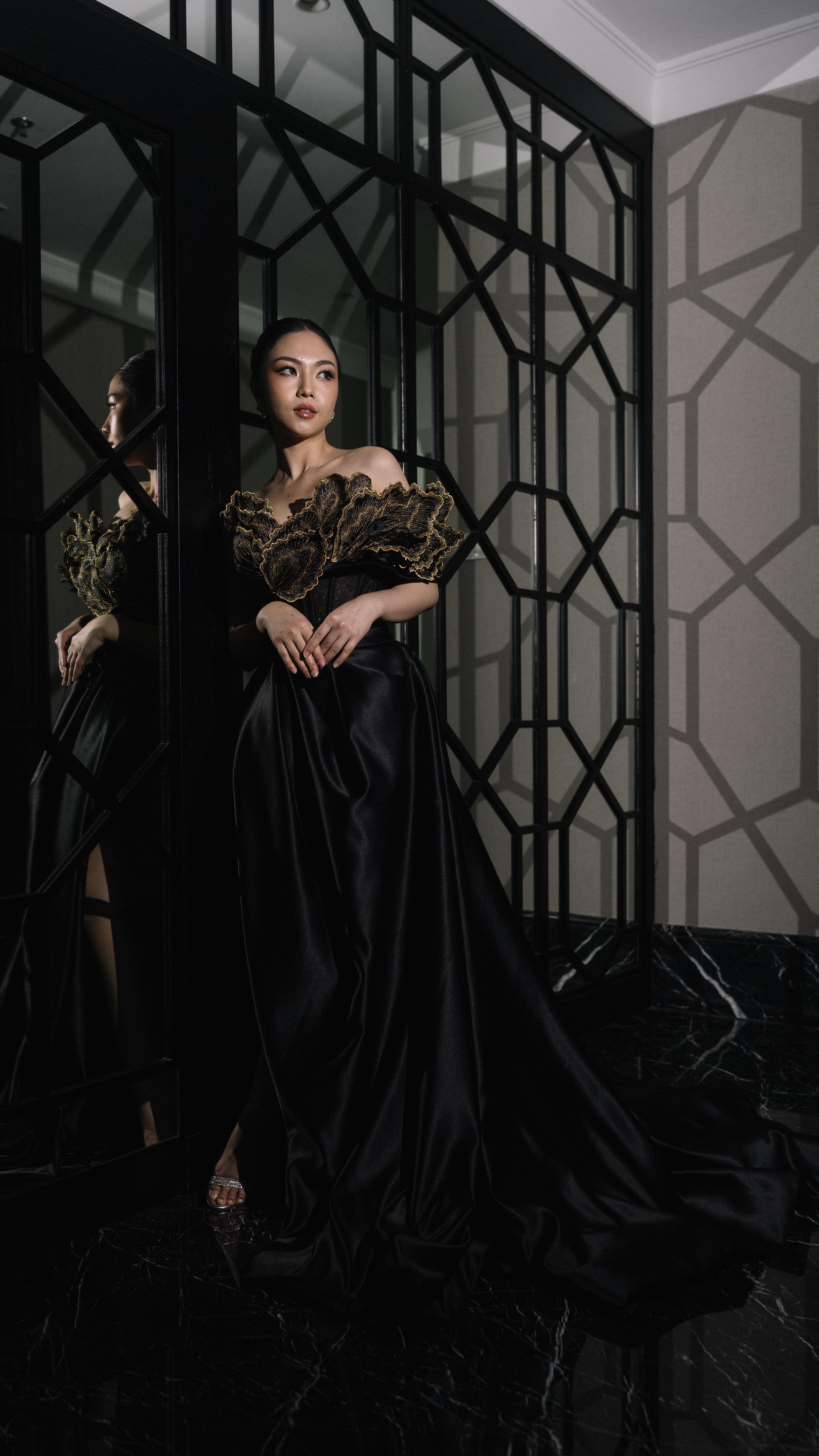 Black satin gown with gold ruffled bodice beside a geometric screen by CELRA