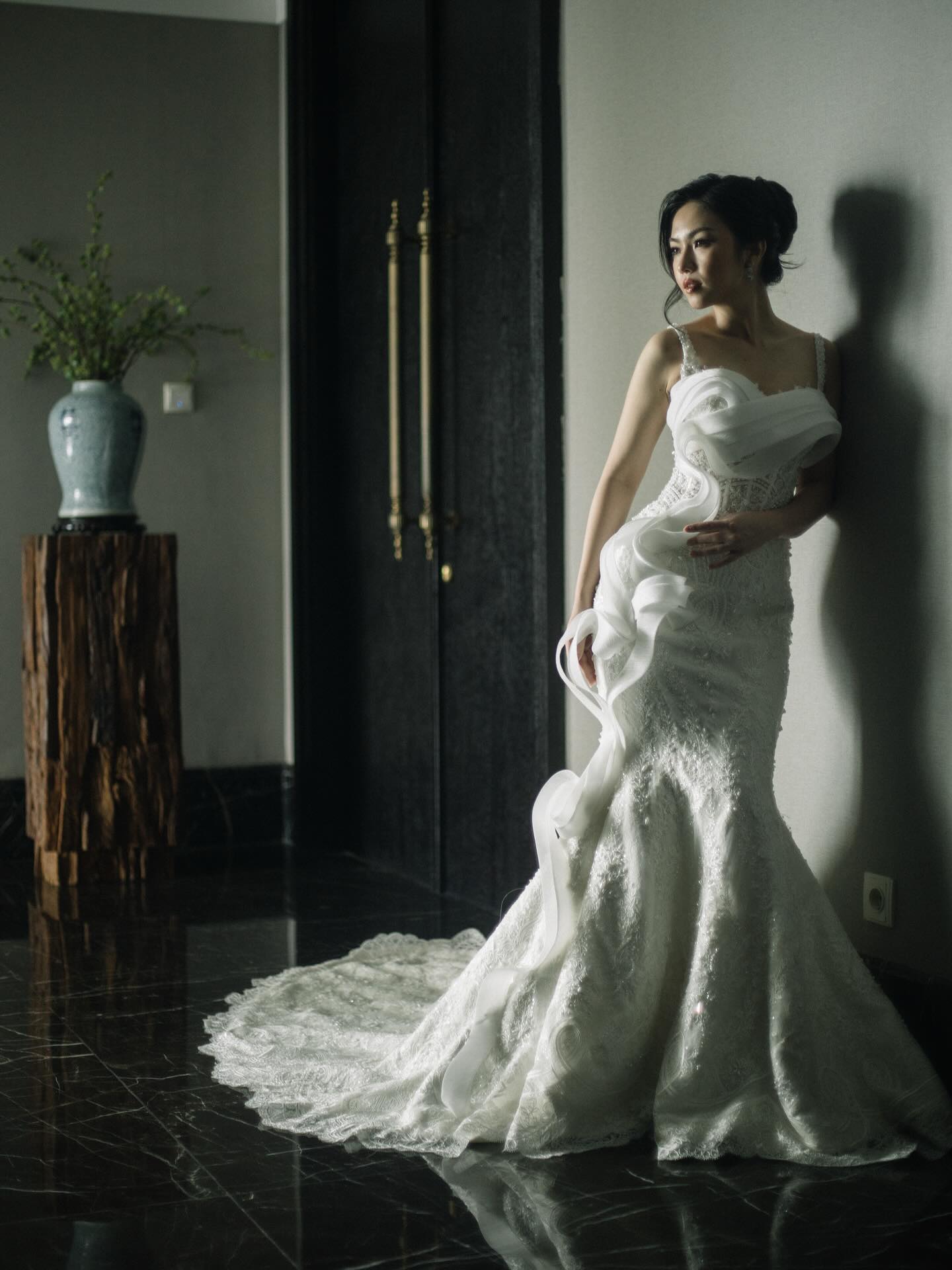 Mermaid wedding gown with cascading ruffles in a dark hallway by CELRA