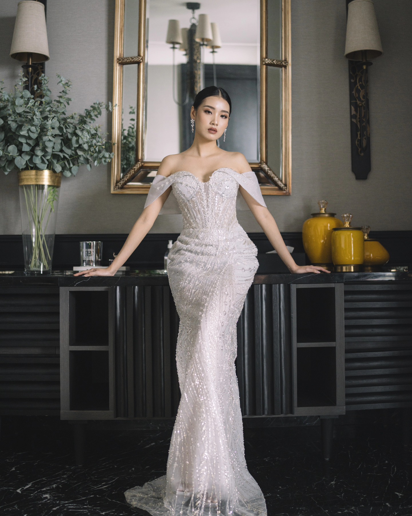 Off-shoulder beaded mermaid gown beside a gilded mirror by CELRA